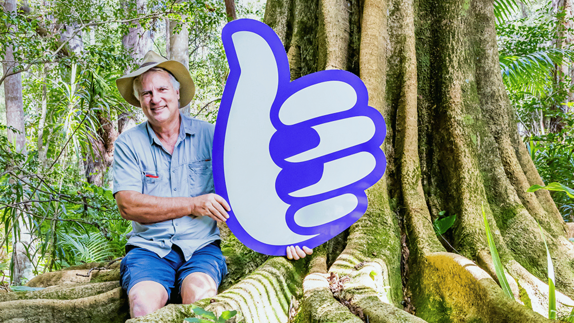 Man holding a Bonza thumb in front of tree at the Coffs Harbour Botanic Gardens.
